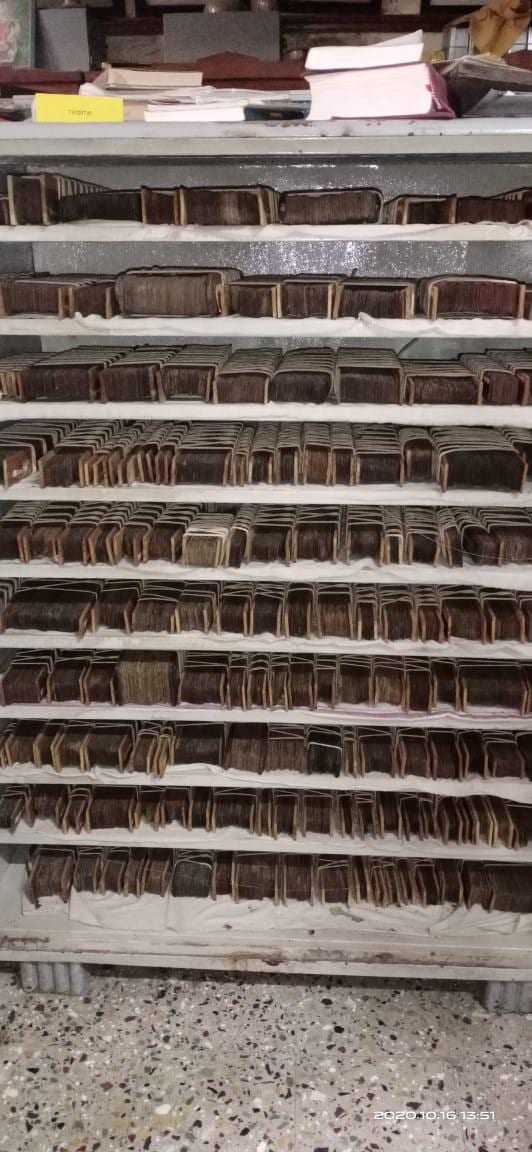 A tall metal rack holding many rows of palm leaf manuscript bundles on cloth-lined shelves.