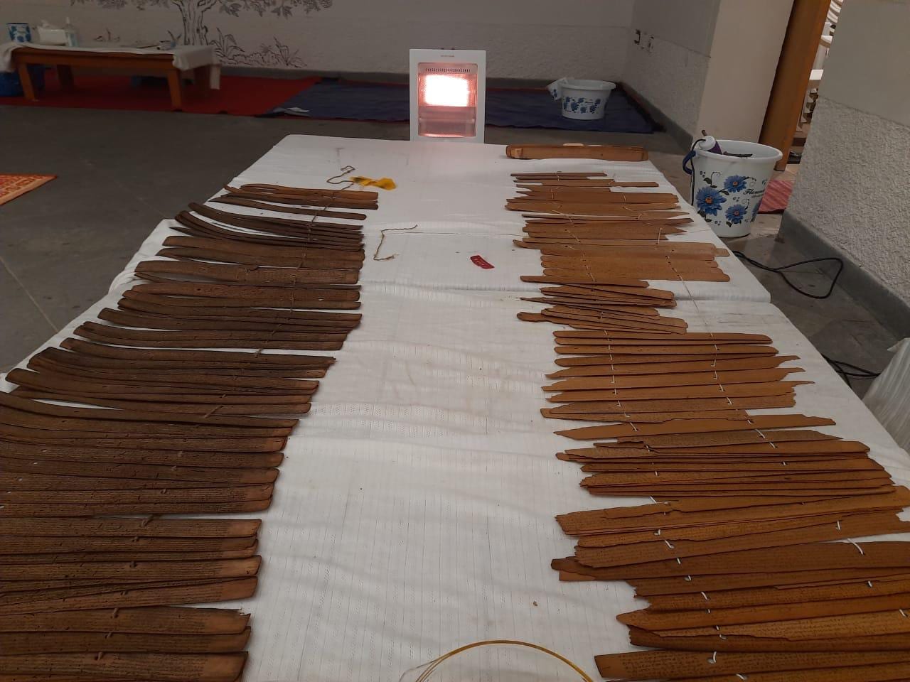 Individual palm leaves spread across a white cloth-covered table with a radiant heater behind them, during the oil treatment stage.