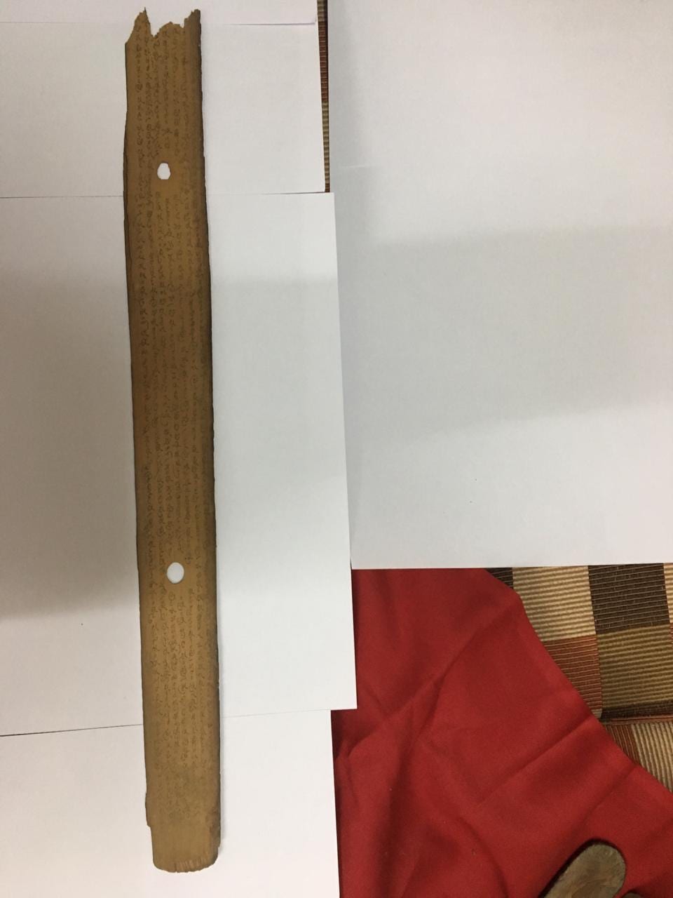 A single restored palm leaf photographed against white paper, its incised script clearly legible along its length, with two binding holes.